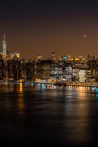 Illuminated buildings by river against sky at night