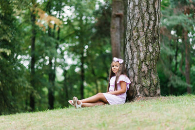 A beautiful little girl sitting near a tree, relaxing, enjoying a sunny day in a green park