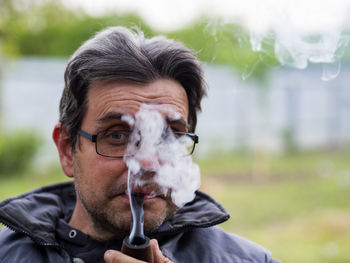 Unshaven caucasian man in glasses smokes a pipe