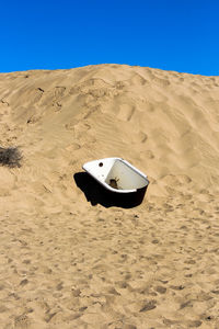 Boat on sand dunes against clear blue sky