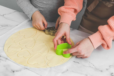 Two caucasian girls cut out shortbread dough with metal and plastic heart shapes.