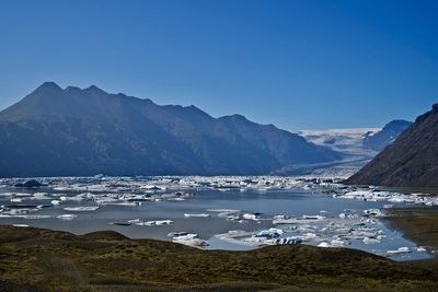 Iceberg filled lagoon at the foot of a glacier, surrounded by mountains on a bright clear day.