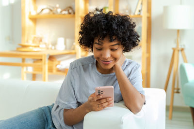 Young woman using mobile phone while sitting on bed at home