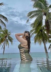 Young woman with arms outstretched on beach against sky