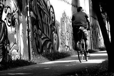 Rear view of man riding bicycle by graffiti wall