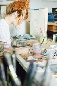 Side view of female artist painting while standing at table in studio