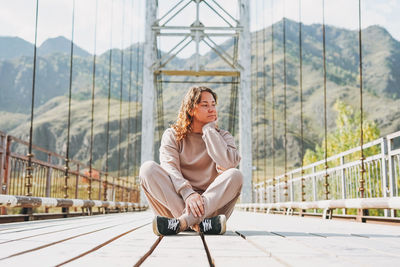 Young woman traveller in casual clothes sitting on horochowski bridge on katun river, altai 