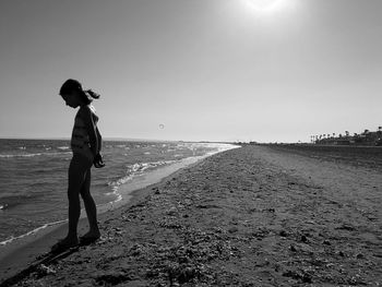 Side view of girl in swimsuit standing on shore at beach against clear sky