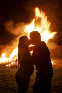 Silhouette couple kissing while standing against bonfire at night