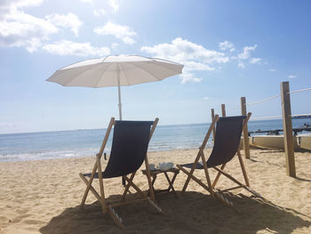 Deck chairs on beach against sky