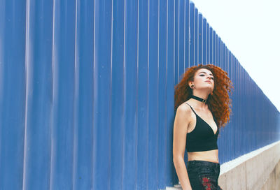 Young woman standing by blue corrugated iron