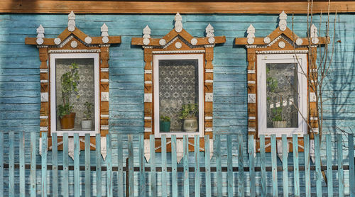 Windows on turquoise plank wall of old house with wooden carved architraves with cracked paint.