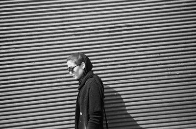 Side view of woman walking by wall on sunny day