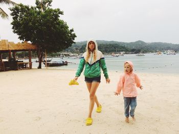 Full length of mother and daughter walking at beach against sky