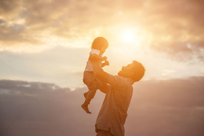 Side view of mother and daughter against sky during sunset