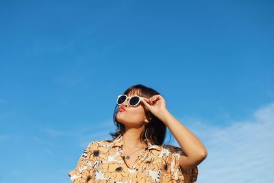 Portrait of woman wearing sunglasses against blue sky