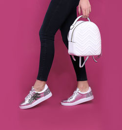 Low section of woman with backpack walking against pink background