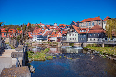 Buildings by river against clear blue sky