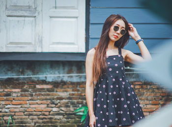 Portrait of young woman wearing sunglasses standing against brick wall