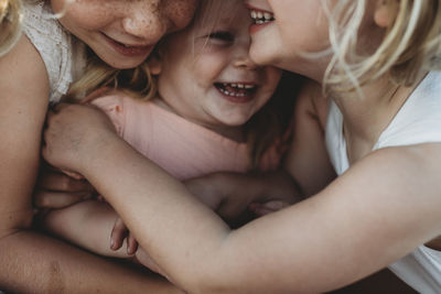 Close up of toddler laughing surrounded by young sisters