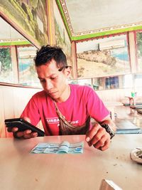 Portrait of young man using mobile phone while sitting on table