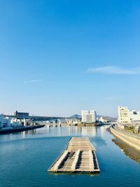 Buildings by river against blue sky