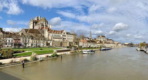View of buildings by river against cloudy sky