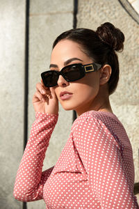 Young woman wearing sunglasses while standing against wall