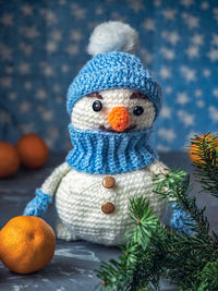 Knitted toys white snowman in a blue hat with a branch of a christmas tree and tangerines