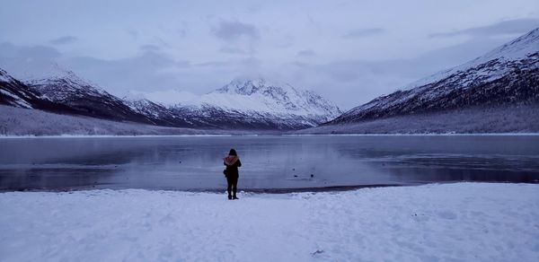 Rear view of woman standing by lake during winter