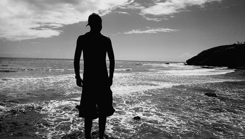 Rear view of silhouette man standing at beach against sky