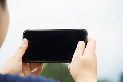 Cropped hands of man holding mobile phone against sky