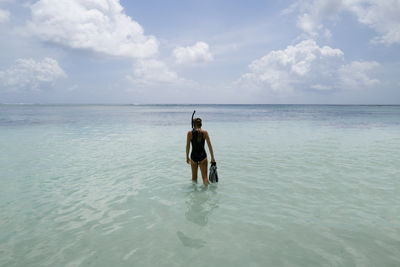 Woman standing in the water wearing wetsuit holding snorkeling equipment