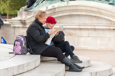 Mother reading map while sitting with daughter on steps