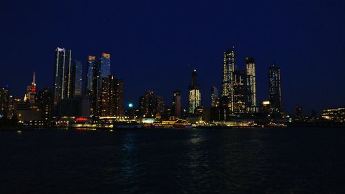 Illuminated buildings by river against sky at night