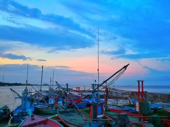 Boats moored at harbor against sky during sunset