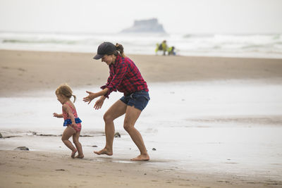 Fit, fun mother playfully chases her young daughter on the beach.