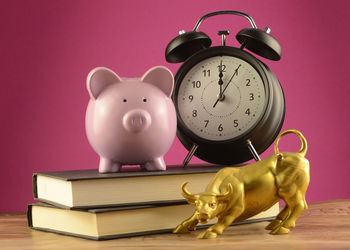 Low angle view of clock on book against pink background