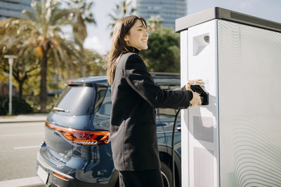 Happy woman charging electric car at charging station