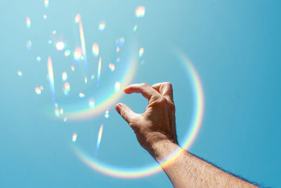 Cropped hand of woman holding sparkler against clear blue sky