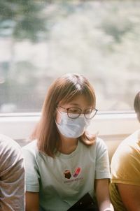 Young woman wearing mask sitting by window