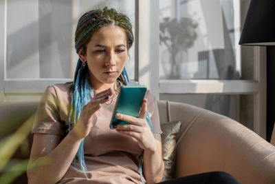 Woman using mobile phone sitting on sofa