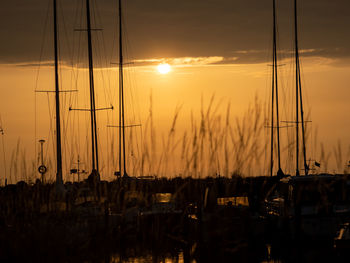 Silhouette sailboats moored at harbor against sky during sunset