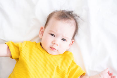 Top view healthy asian baby girl 5 months in yellow bodysuit on bed on white bedding