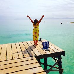 Rear view of woman standing on pier over sea against sky