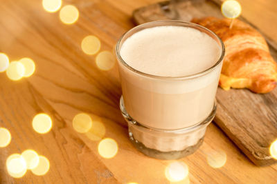 A cup of cappuccino and a hot croissant on a wooden table