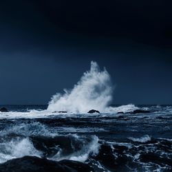 Sea waves splashing on rocks against sky at dusk