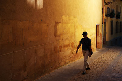 Rear view of man walking on footpath amidst buildings