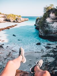 Low section of man sitting on rock at beach against sky