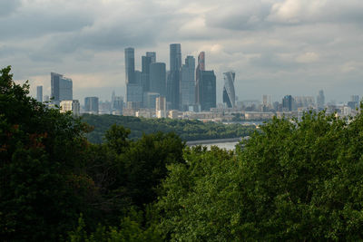 Trees and buildings in city against sky